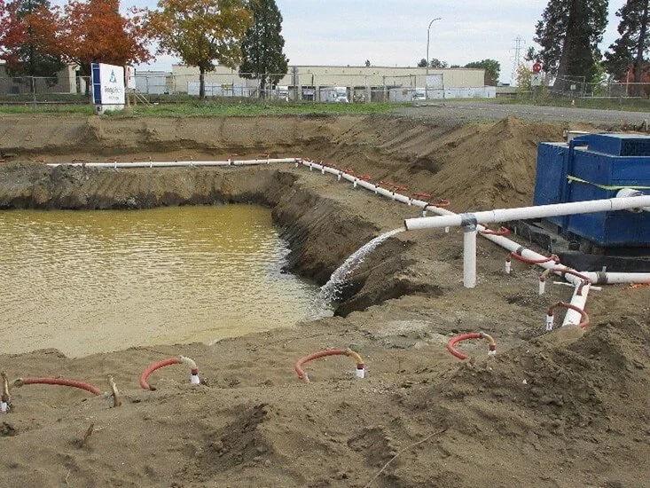 Pond excavation project with white discharge pipes and red hoses managing water flow during active earthwork.